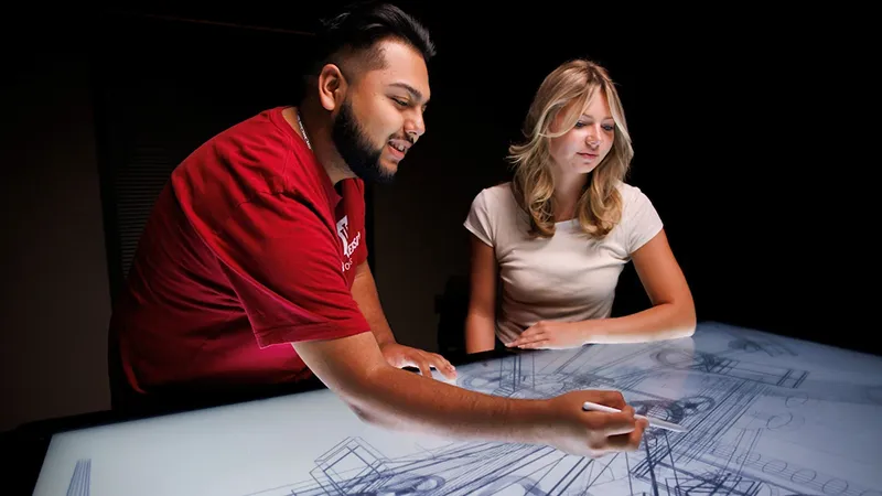 A male and female collaborate on architectural sketches at a drafting table.